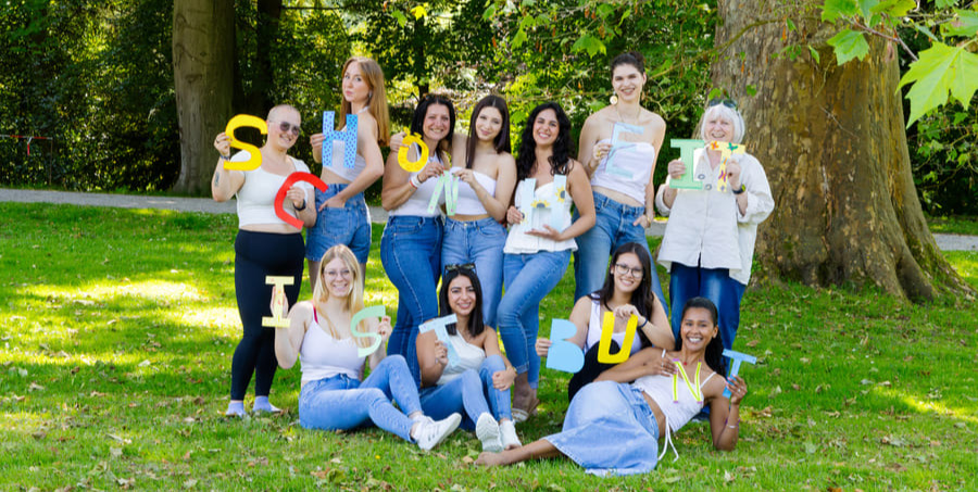 Ehrenamtsteam von Love Always Wins e.V. hält bunte Buchstaben mit der Botschaft „Schule ist bunt“ im Park