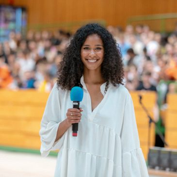 Lijana Kaggwa bei Schulvortrag – Love Always Wins e.V. Lijana Kaggwa hält ein Mikrofon bei einem Vortrag vor Schülern – Love Always Wins e.V. engagiert gegen Cybermobbing